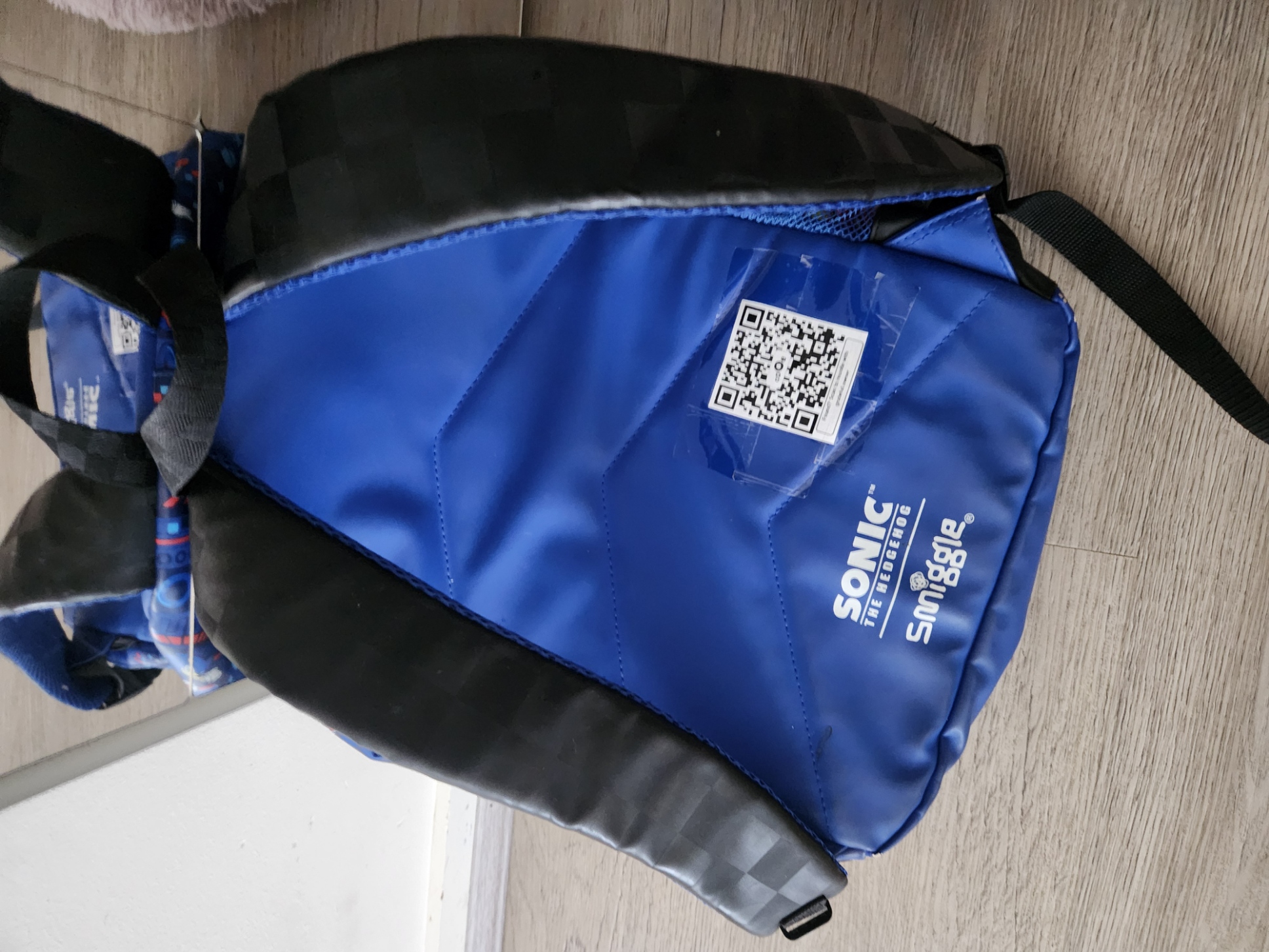 QR code label attached to blue and black Smiggle school bag with clear tape, showing the Sonic branding and QR code clearly visible